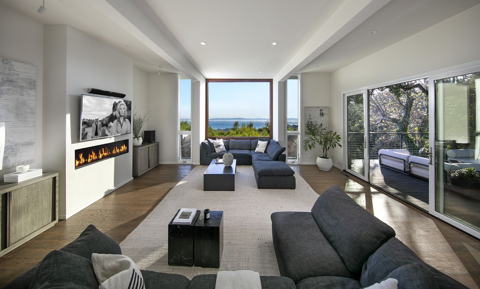 A luxury family room with a contemporary-style gas fireplace, comfy furniture and a window that looks out to the ocean.