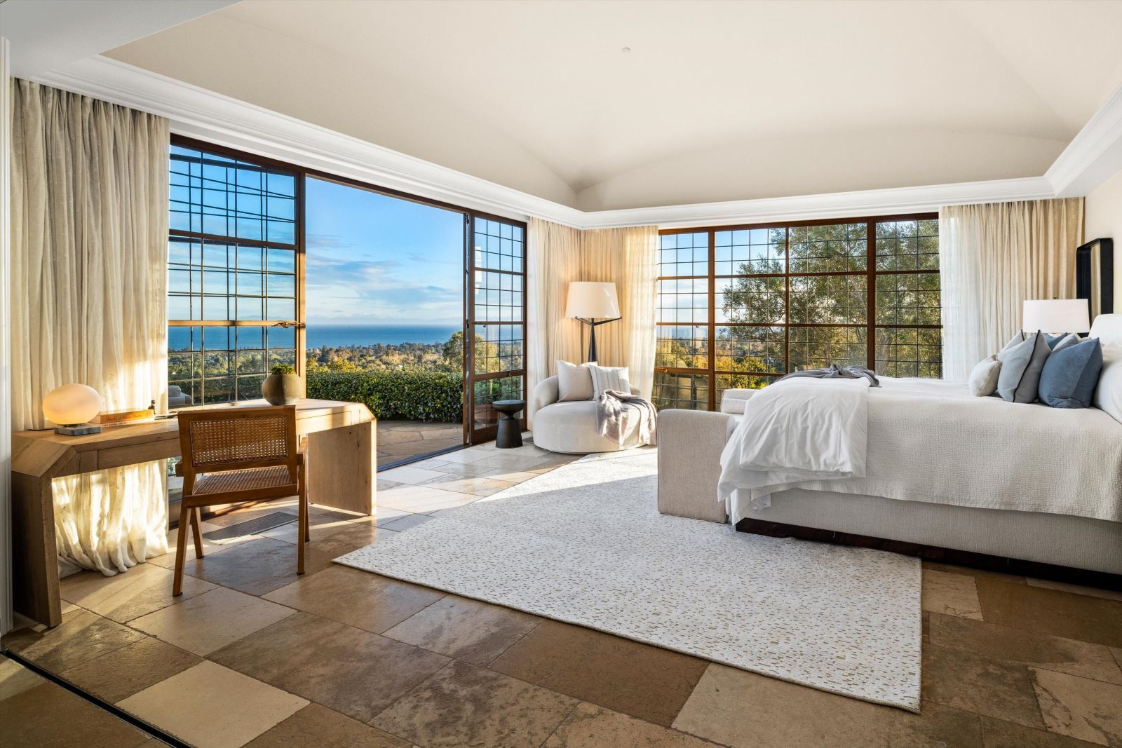 A luxury primary suite with window paneled door open to reveal ocean views.