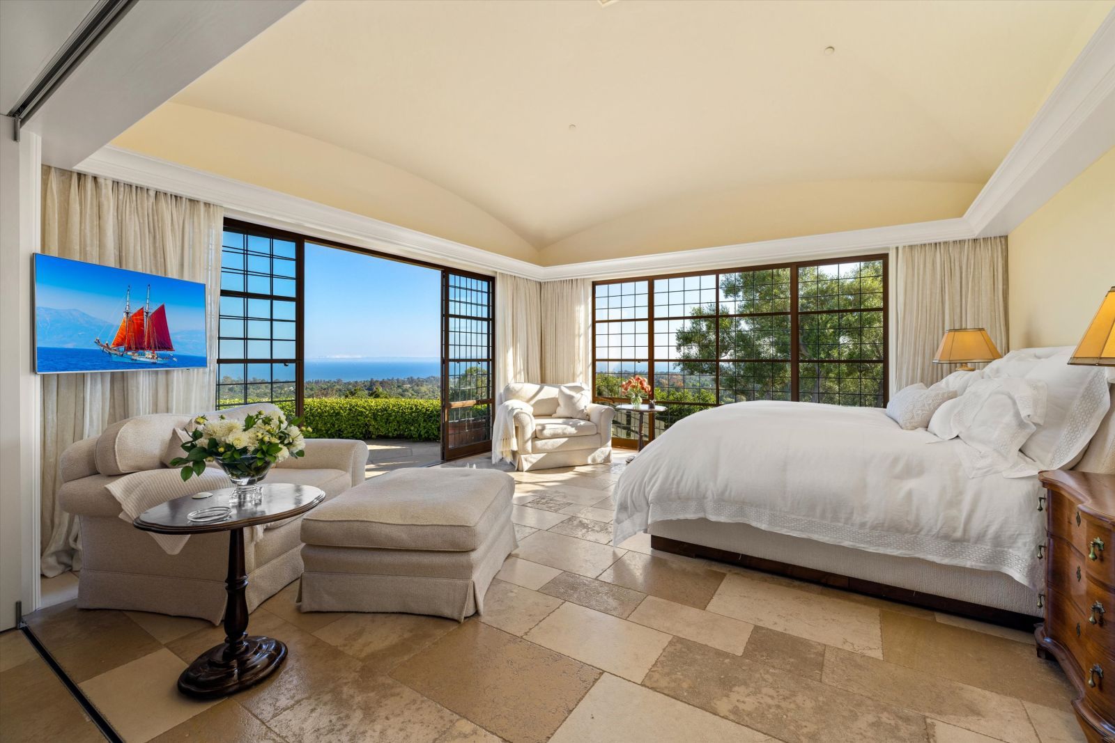 Primary bedroom of a luxury Montecito home, with a plush bed and walls of multi-pane glass looking out to the ocean