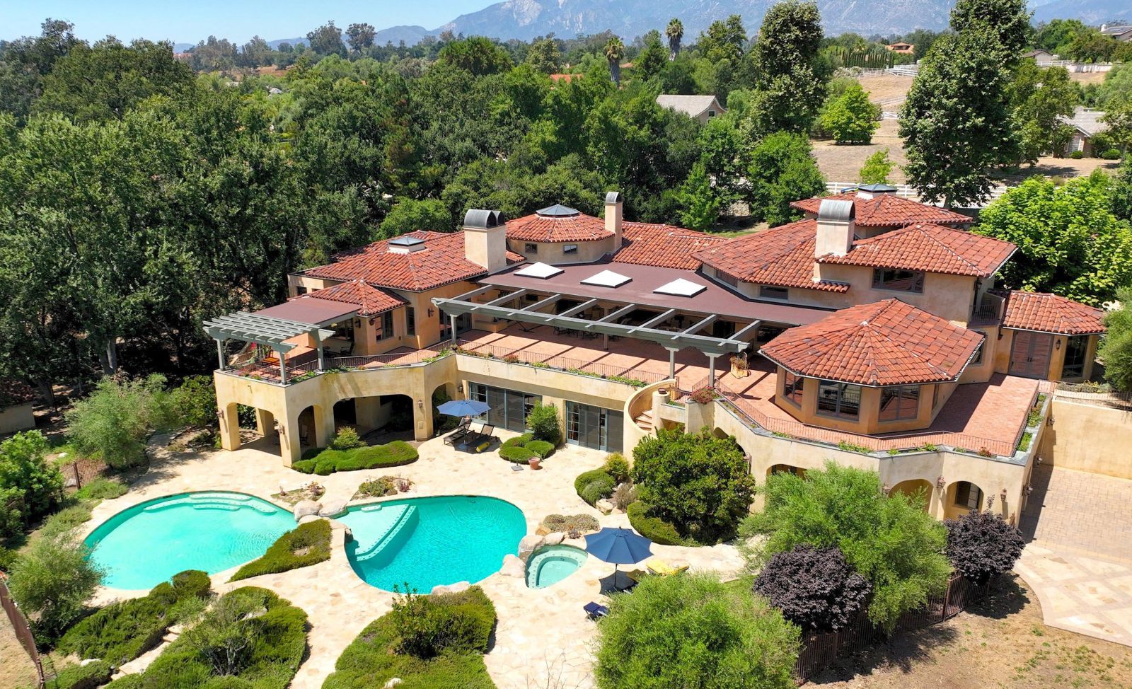 A drone view of an Ojai estate's large Mediterranean-style home, 2 pools, and grounds