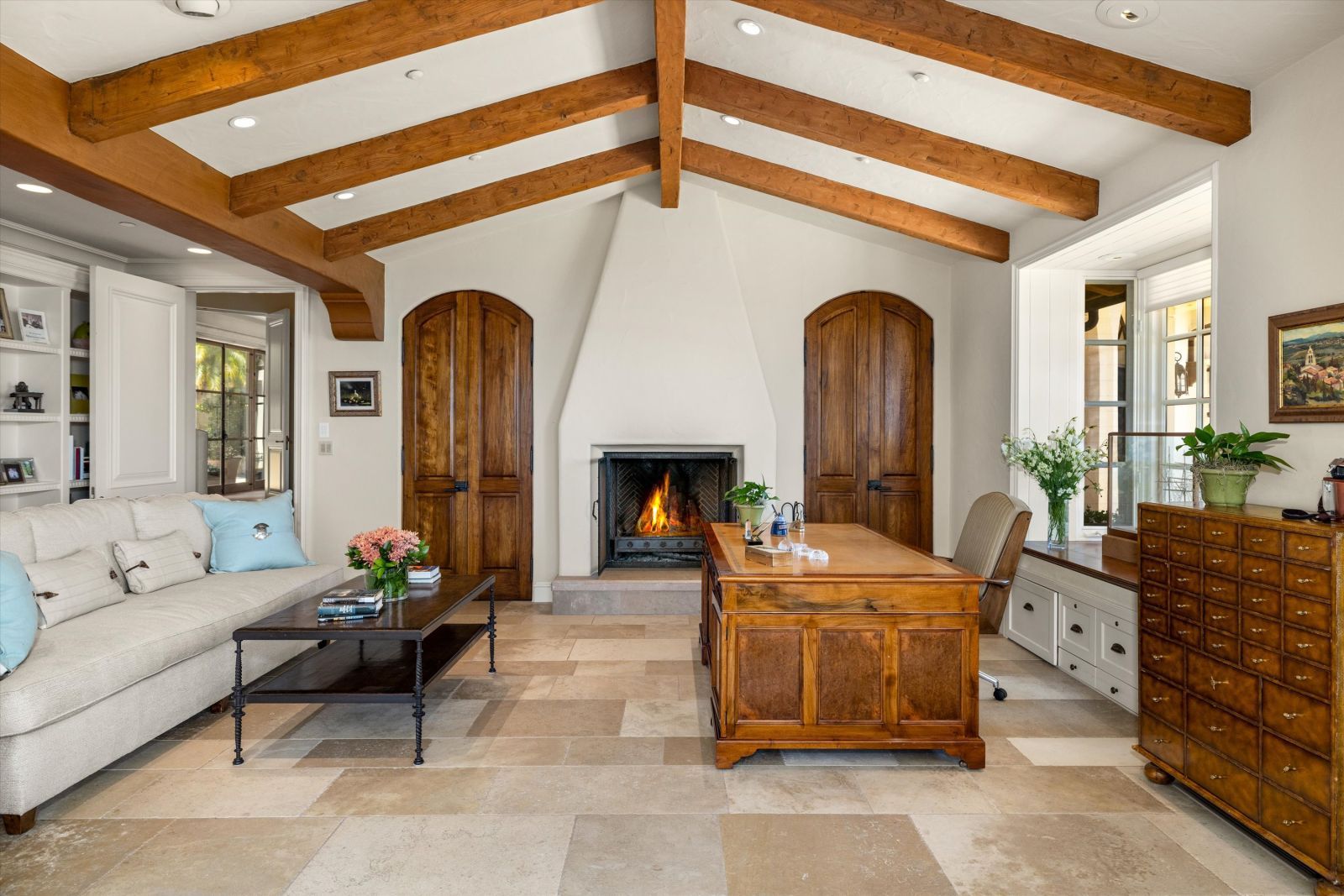 Home office with a fire in the fireplace and an open-beam vaulted ceiling.