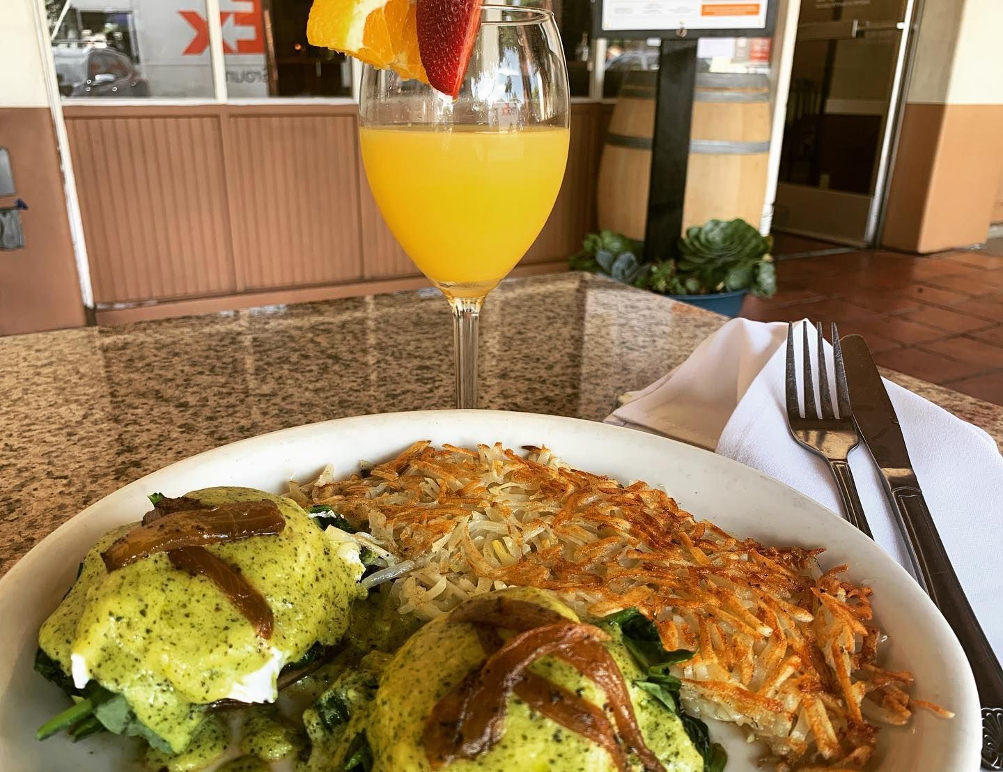 Eggs Benedict with green Hollandaise sauce and a side of hashbrown potatoes and glass of orange juice