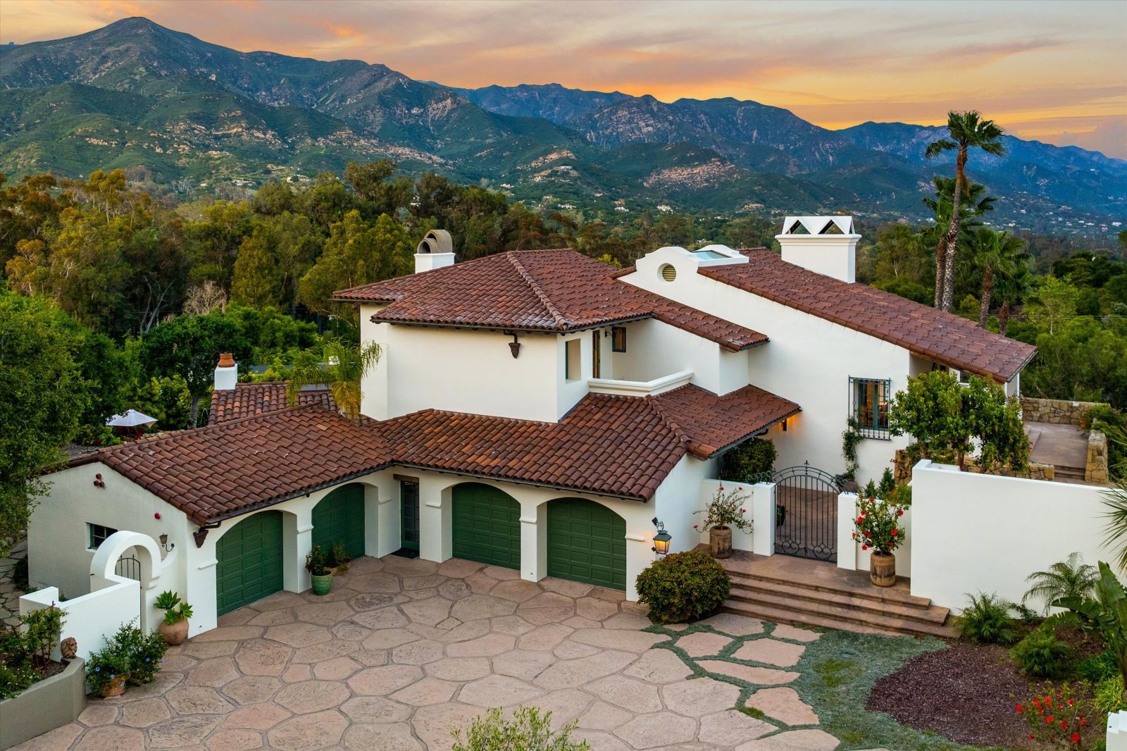 A Spanish Colonial Revival-style home with a red tiled roof framed by mountains and a beautiful yellow and gold sky