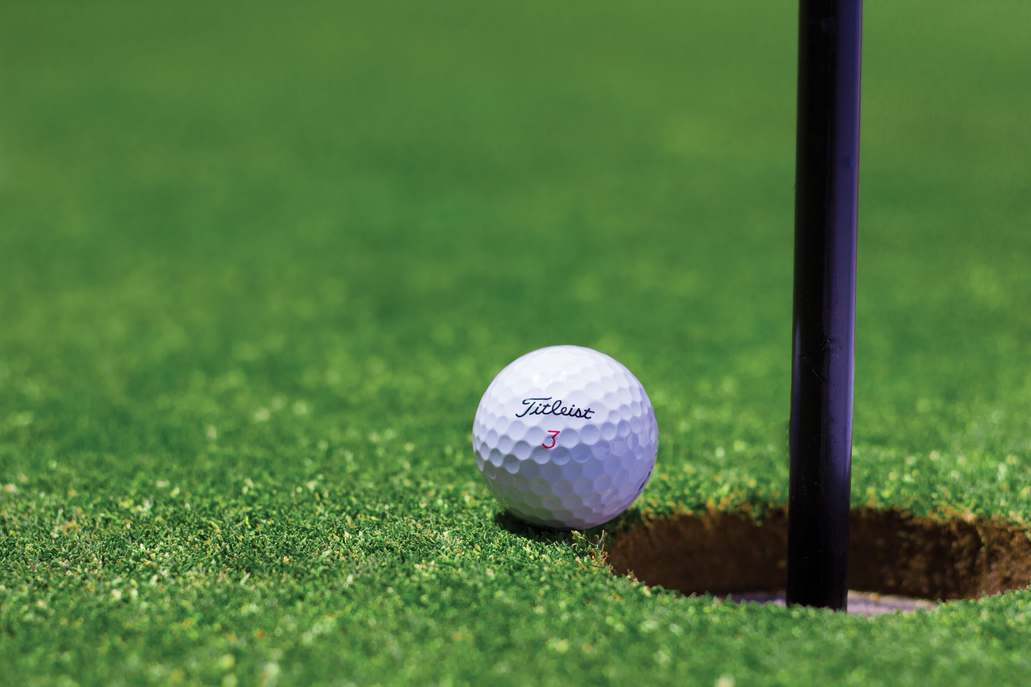 A Titleist golf ball on the green sitting on the lip of the cup on one of Santa Barbara's golf courses