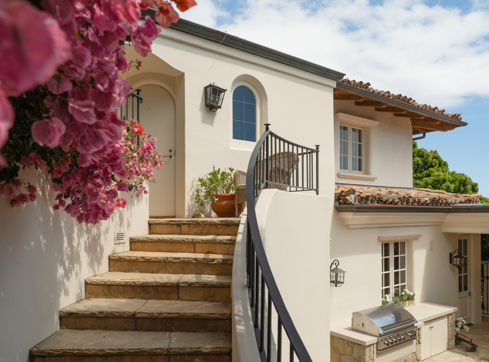 Private guest house entrance with curved wrought-iron staircase, stone steps, Mediterranean-style architecture, blooming bougainvillea, and a separate entry providing privacy for guests or extended family.  I prefer this response