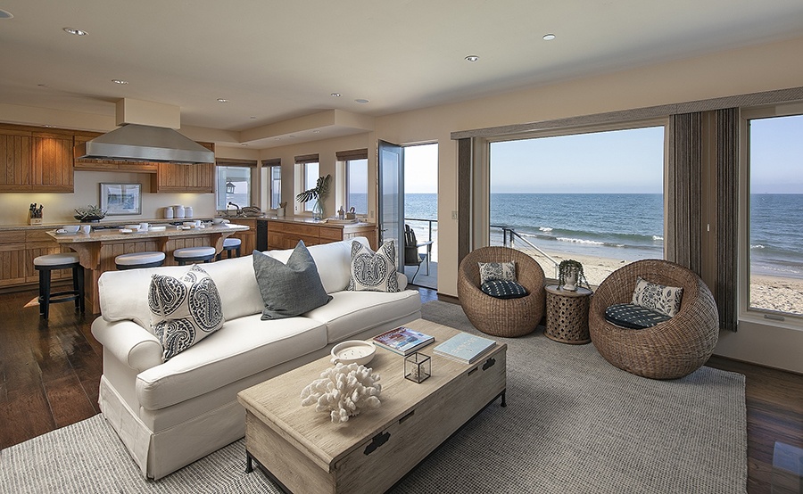 The living room of a luxury home for sale that sits right on the sand with ocean views from every window.