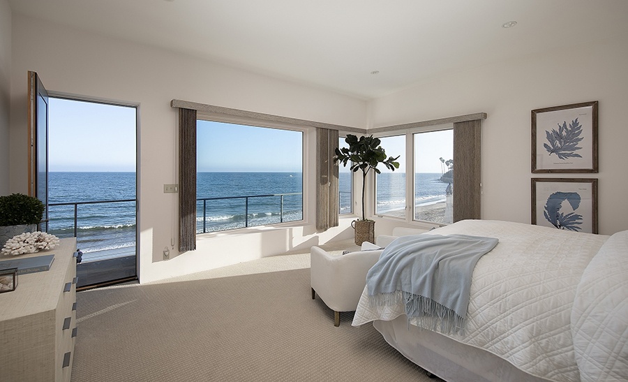 The primary bedroom inside a luxury home complete with a view of the sparking ocean just outside