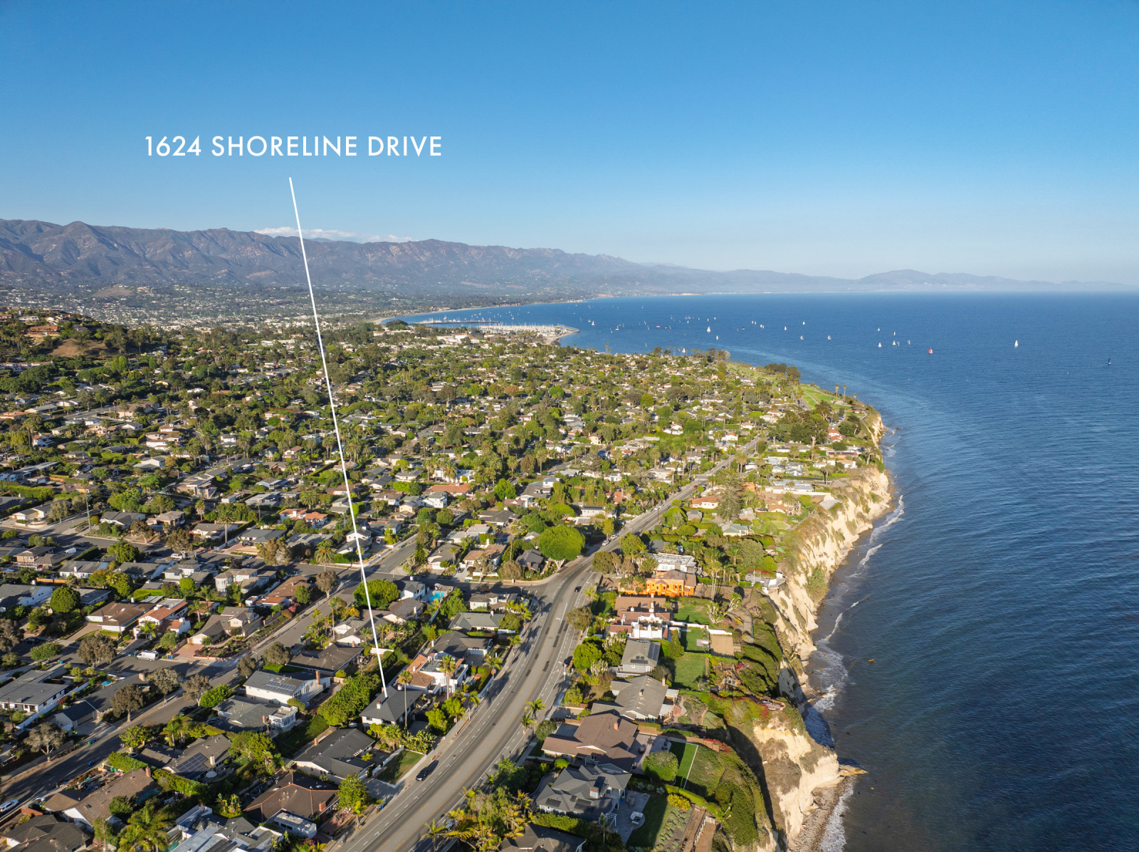Aerial view of the Santa Barbara coastline showing Shoreline Drive, oceanfront homes, dramatic coastal bluffs, the Pacific Ocean, and the Santa Barbara Harbor, with a marker identifying the location of 1624 Shoreline Drive.