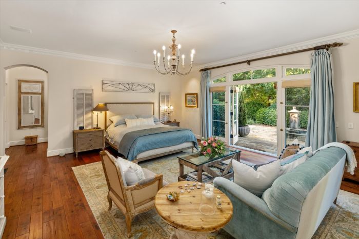 A luxuxurious primary suite in a Montecito home with a chandelier and stylish furniture and French Doors that lead to a private balcony.