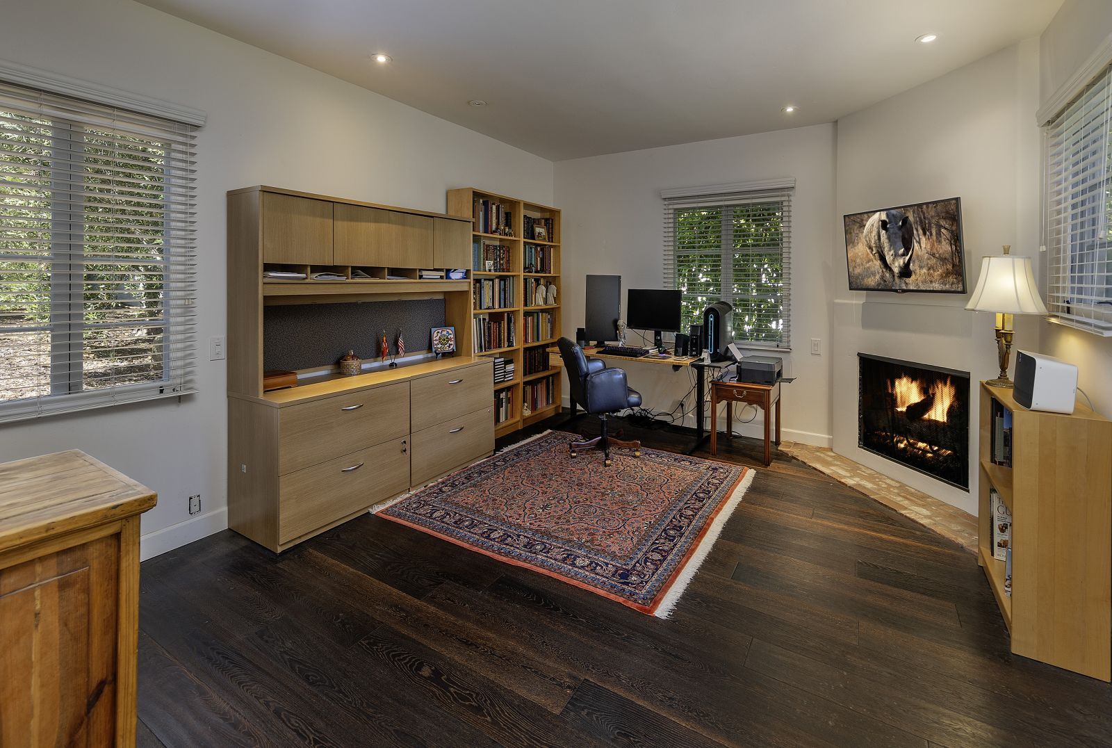 a remote working office setup, with a desk, bookcases, fire in a fireplace, and windows to the garden