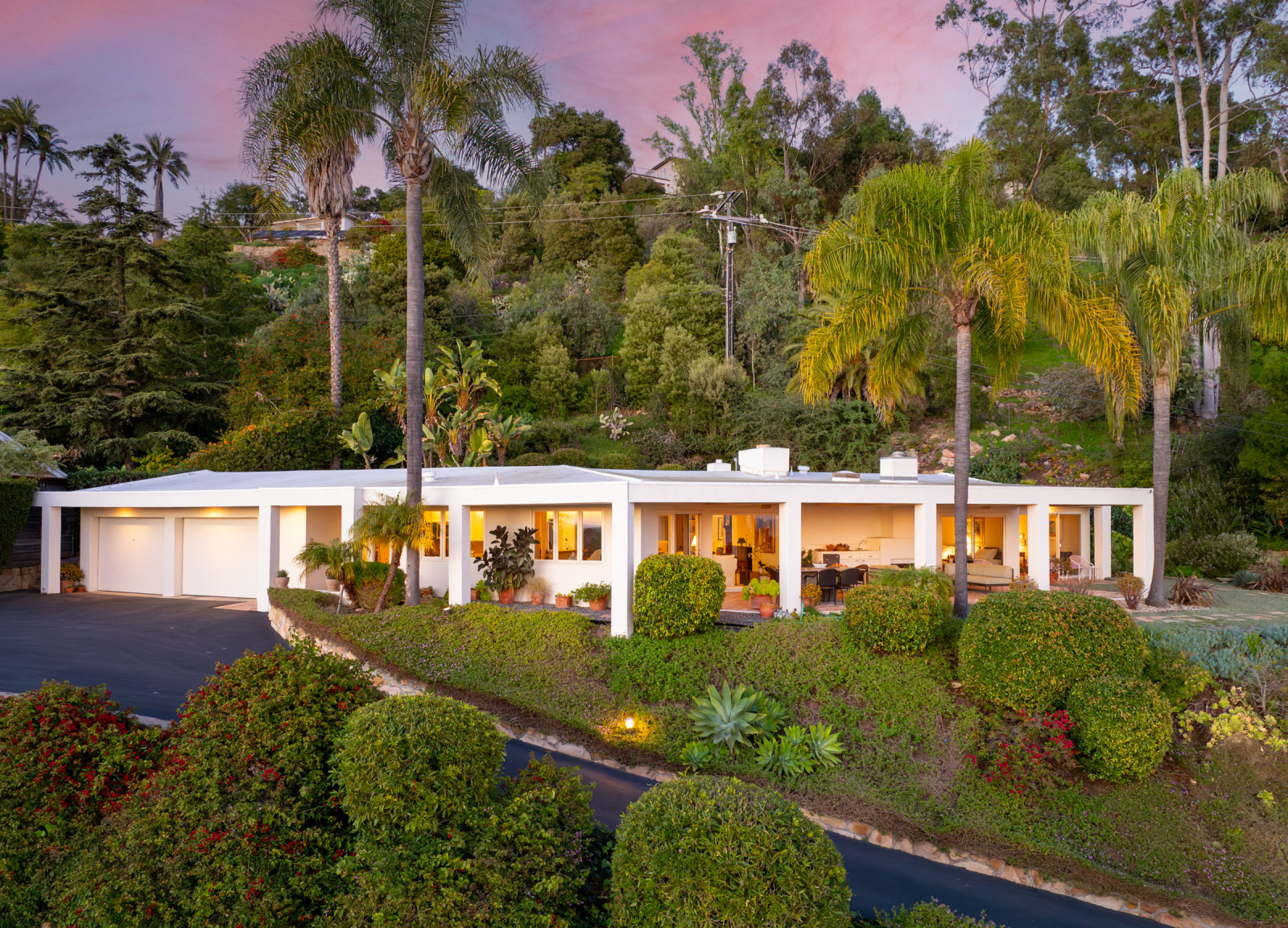 Modern Santa Barbara hillside home with clean lines, lush tropical landscaping, palm trees, and indoor-outdoor living spaces at sunset