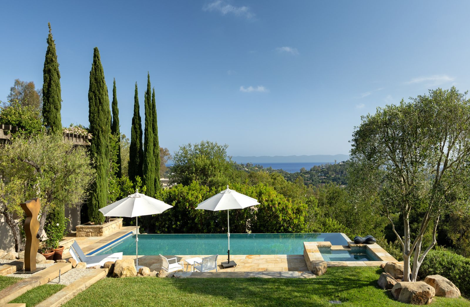 A serene pool overlooking the ocean surrounded by lush landscaping.
