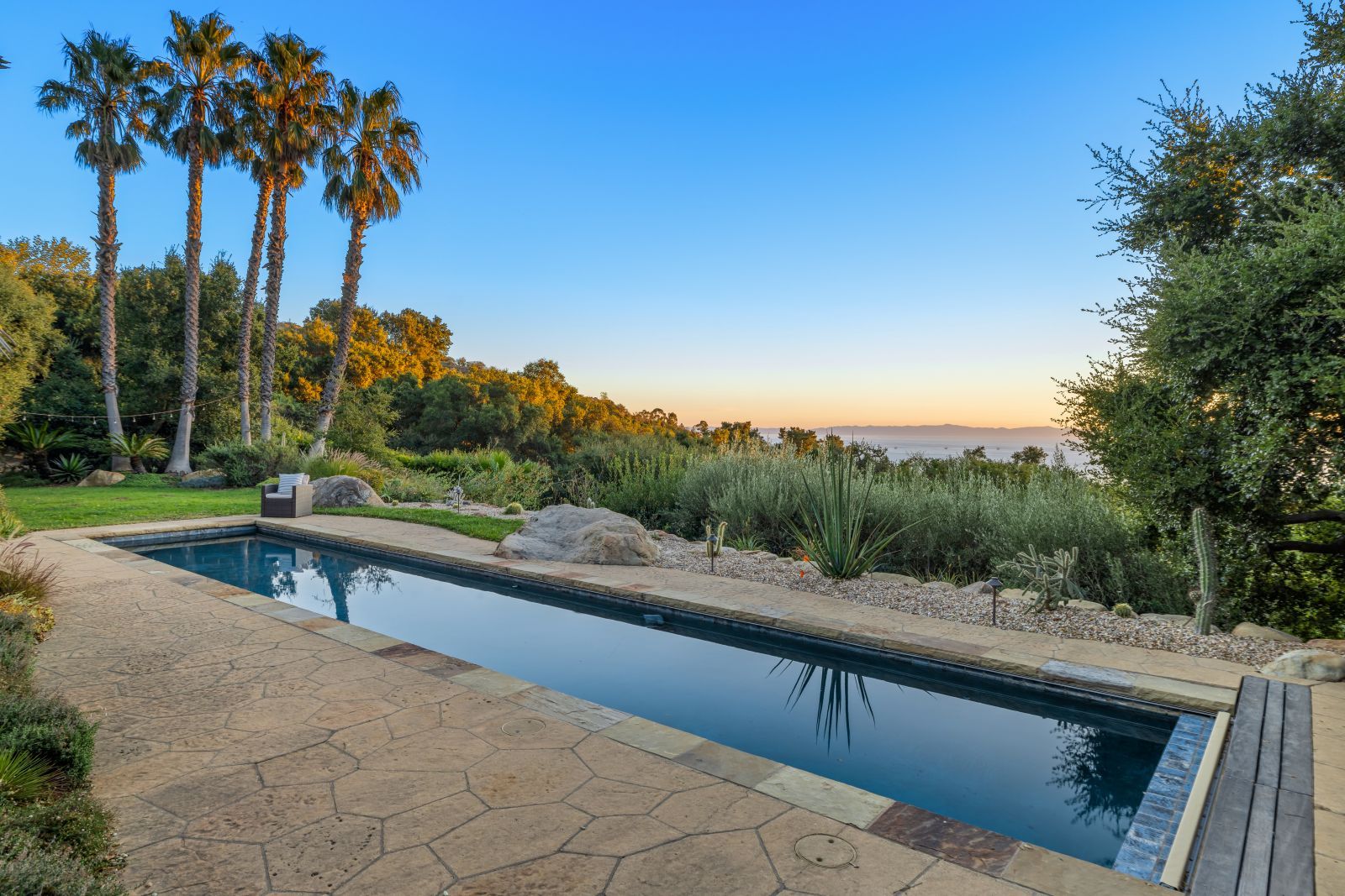 A sparkling pool at sunset with several palm trees, and the ocean in the background