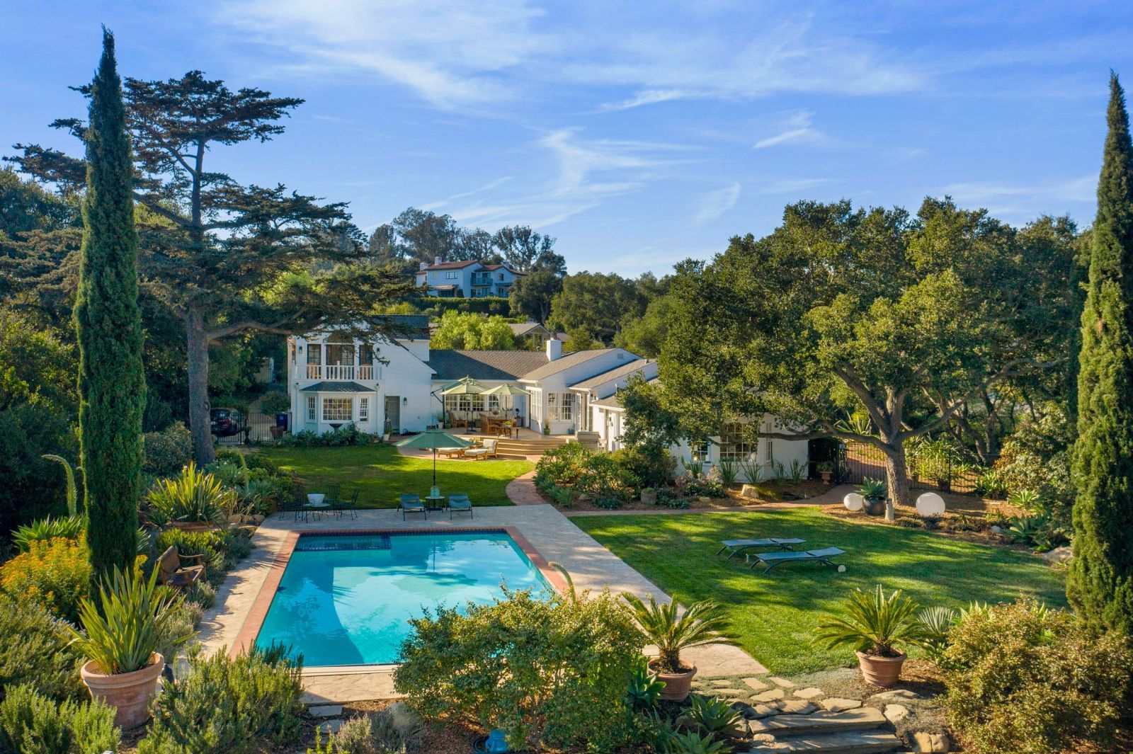 A romantic Cape Cod style Montecito home with lots of greenery, a pool, a sizable lawn with a blue sky in the background