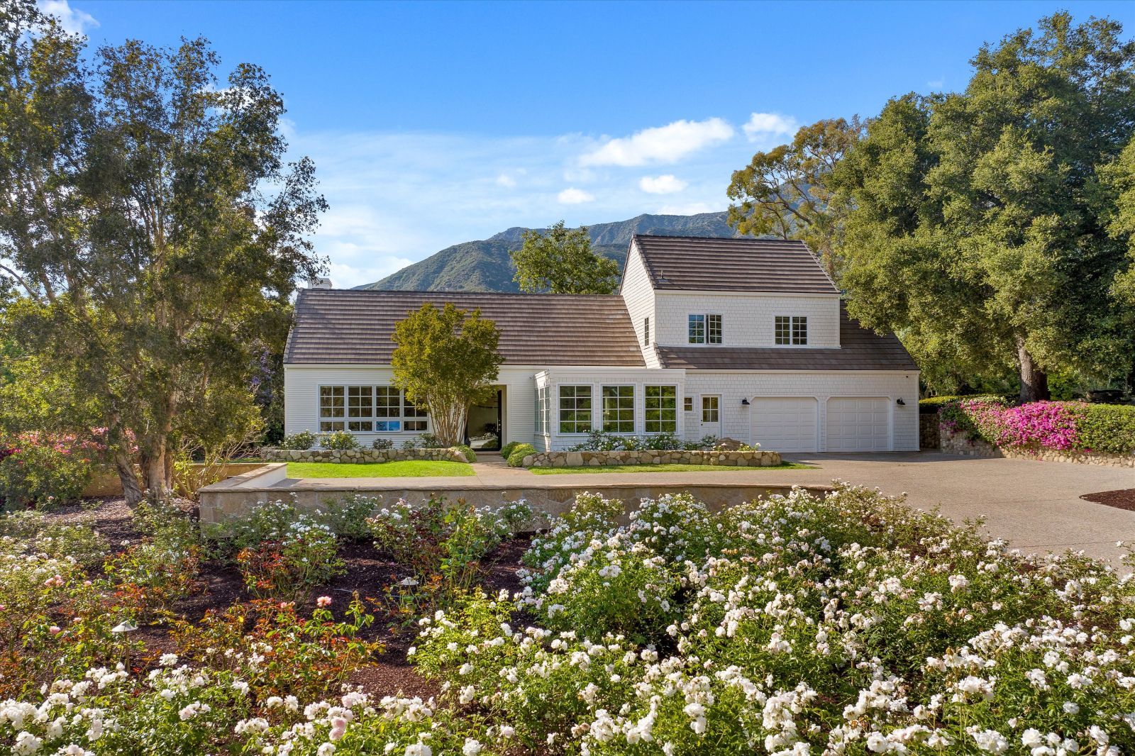 A Cape-Cod style home in Montecito surrounded by lush greenery and mountains in the background.