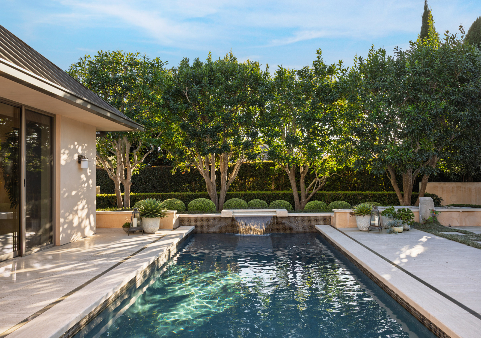 Modern Santa Barbara backyard featuring a resort-style swimming pool, waterfall feature, manicured landscaping, and seamless indoor-outdoor living design.