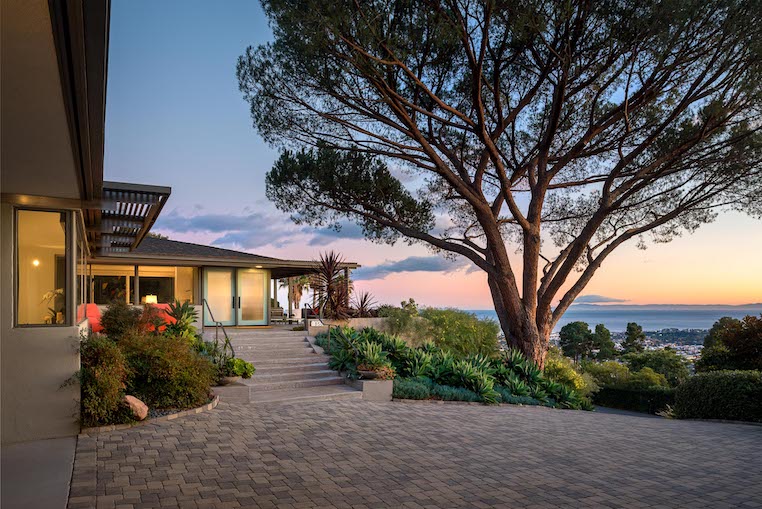 Big beautiful tree in front of a mid century modern home with the ocean in the background