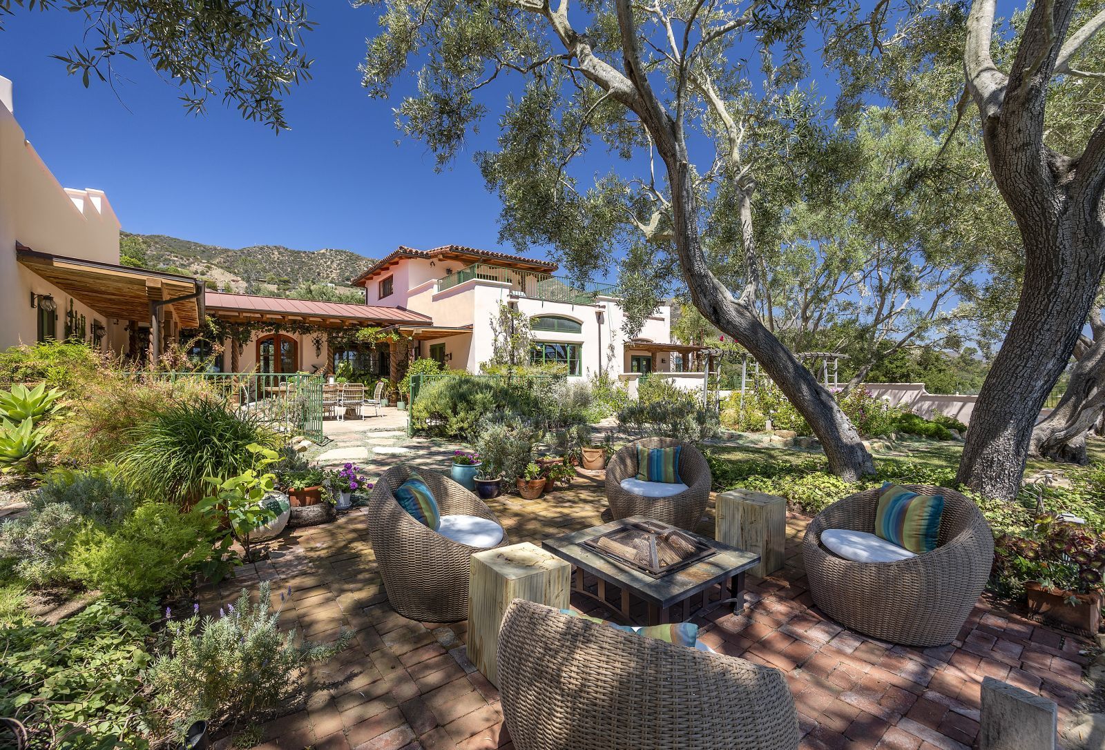 The lush backyard of a Spanish hacienda in Montecito CA, with a large tree, beautiful landscaping, walking paths, and the home in the bakground