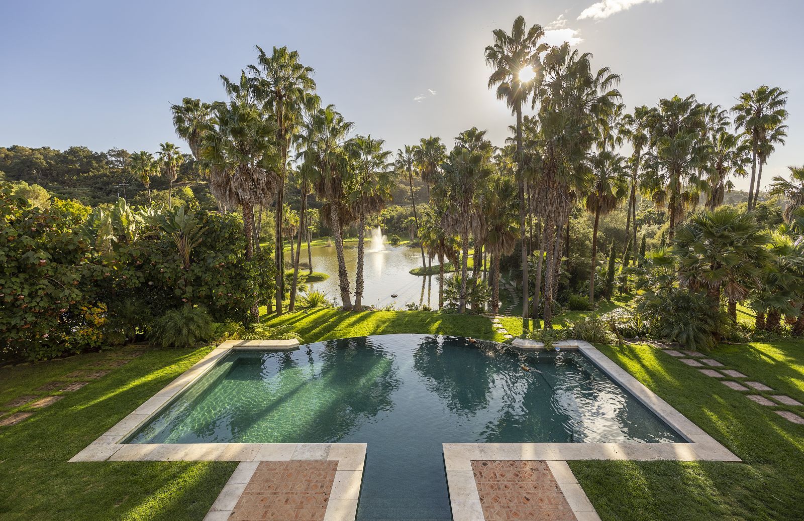 Palm trees stand tall at the foot of a pool that overlooks a substantial pond.