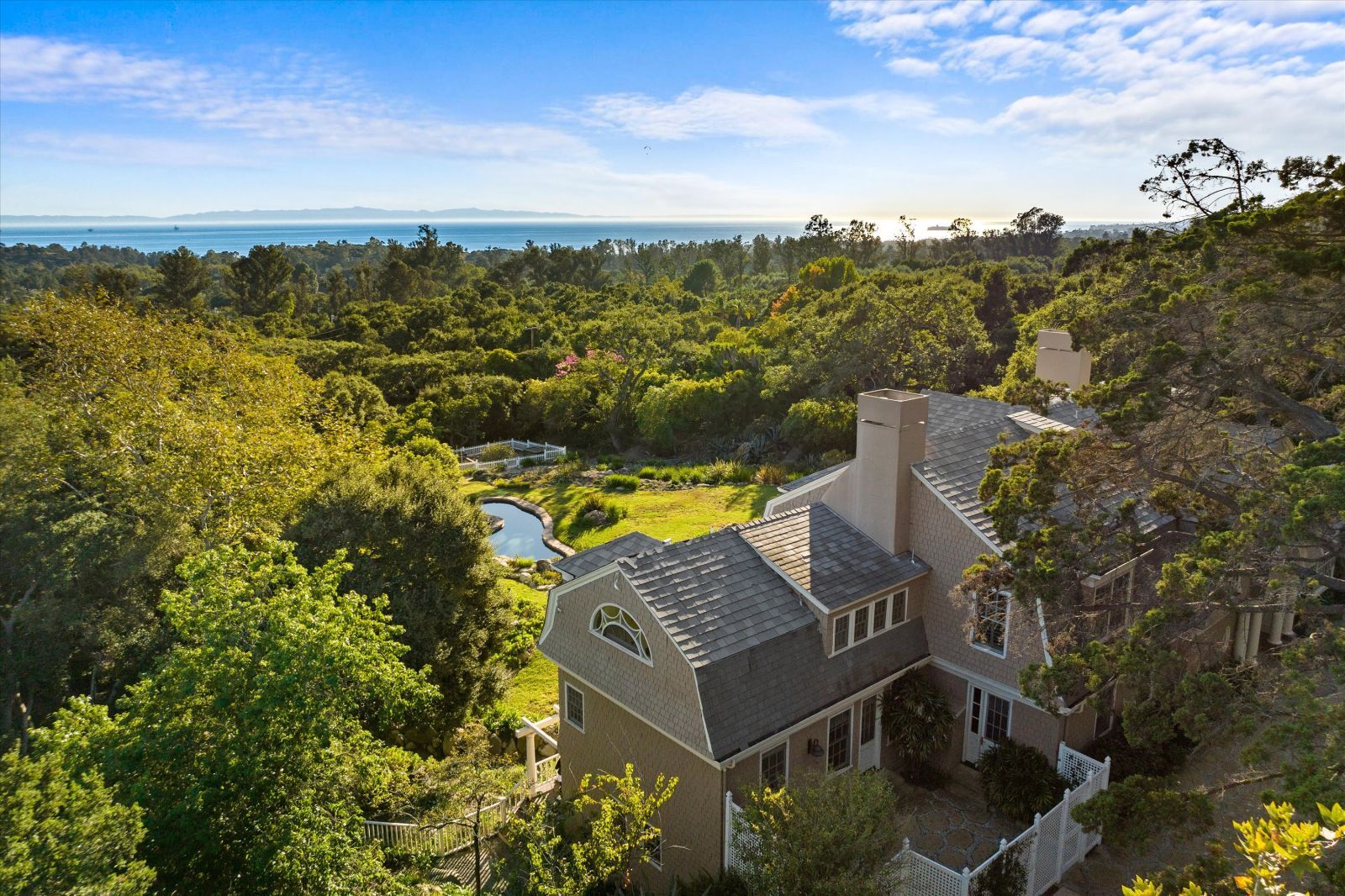 A birds eye view of a Cape Cod style estate in Montecito showcasing the lush backyard and the ocean view.