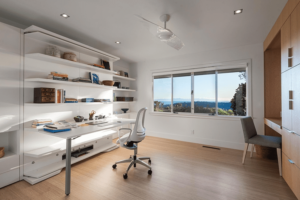 Windows frame a beautiful home office complete with built in shelves and wood floors.