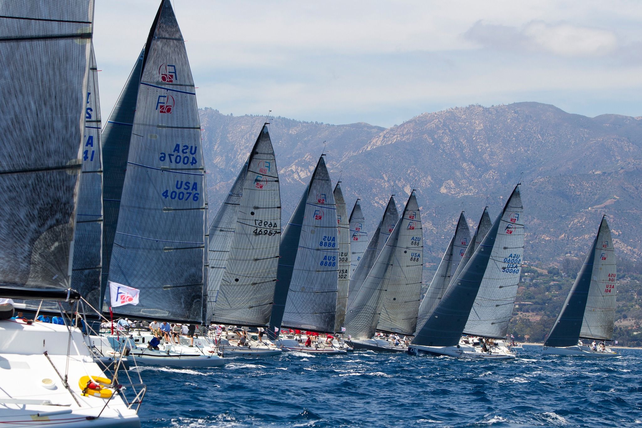 A half-dozen sailboats at full sail competing in a yacht race in the Santa Barbara harbor.