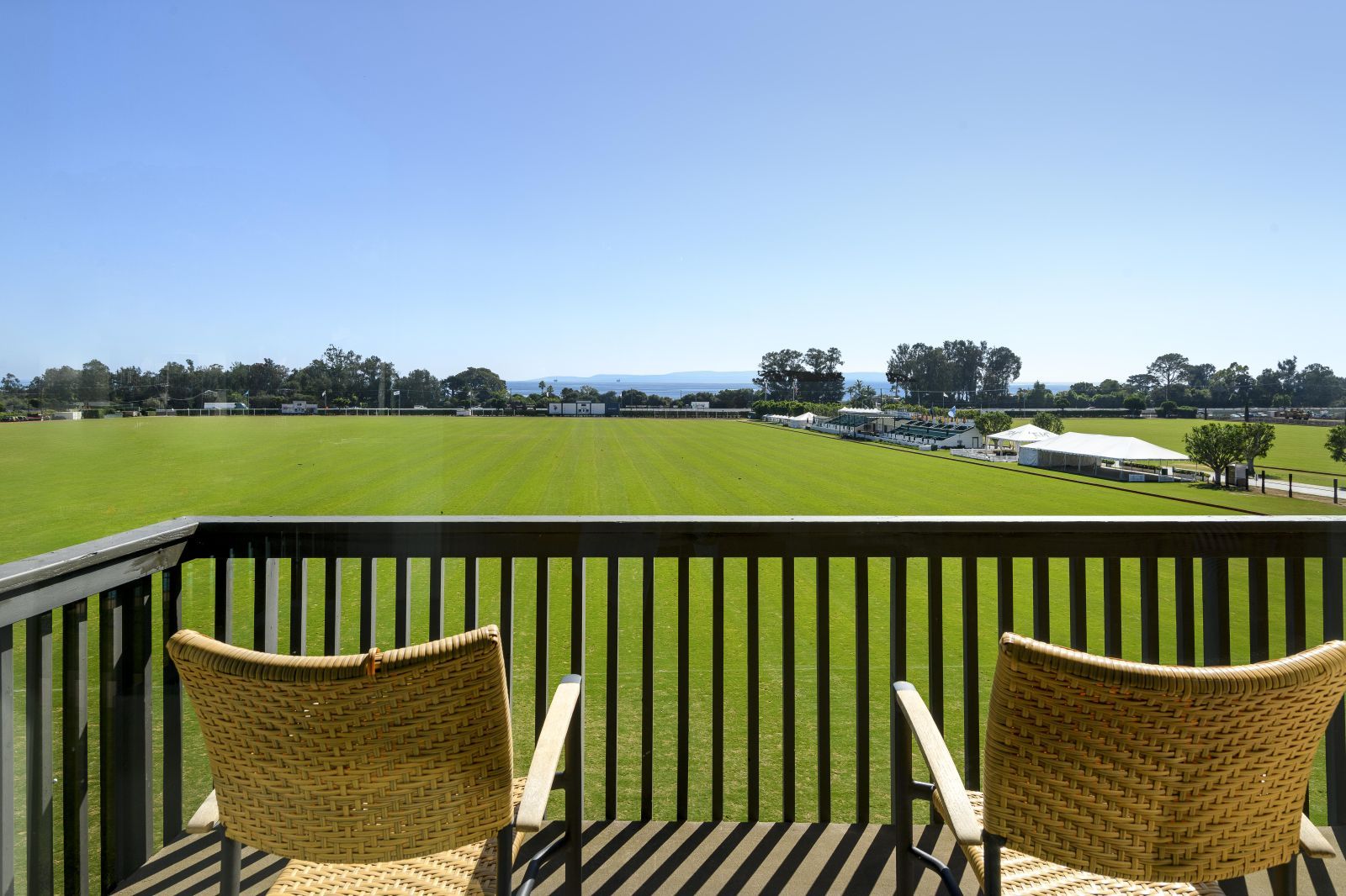 Two chairs sit on a luxury Carpinteria condo with a view of the Santa Barbara Polo field and the ocean beyone.