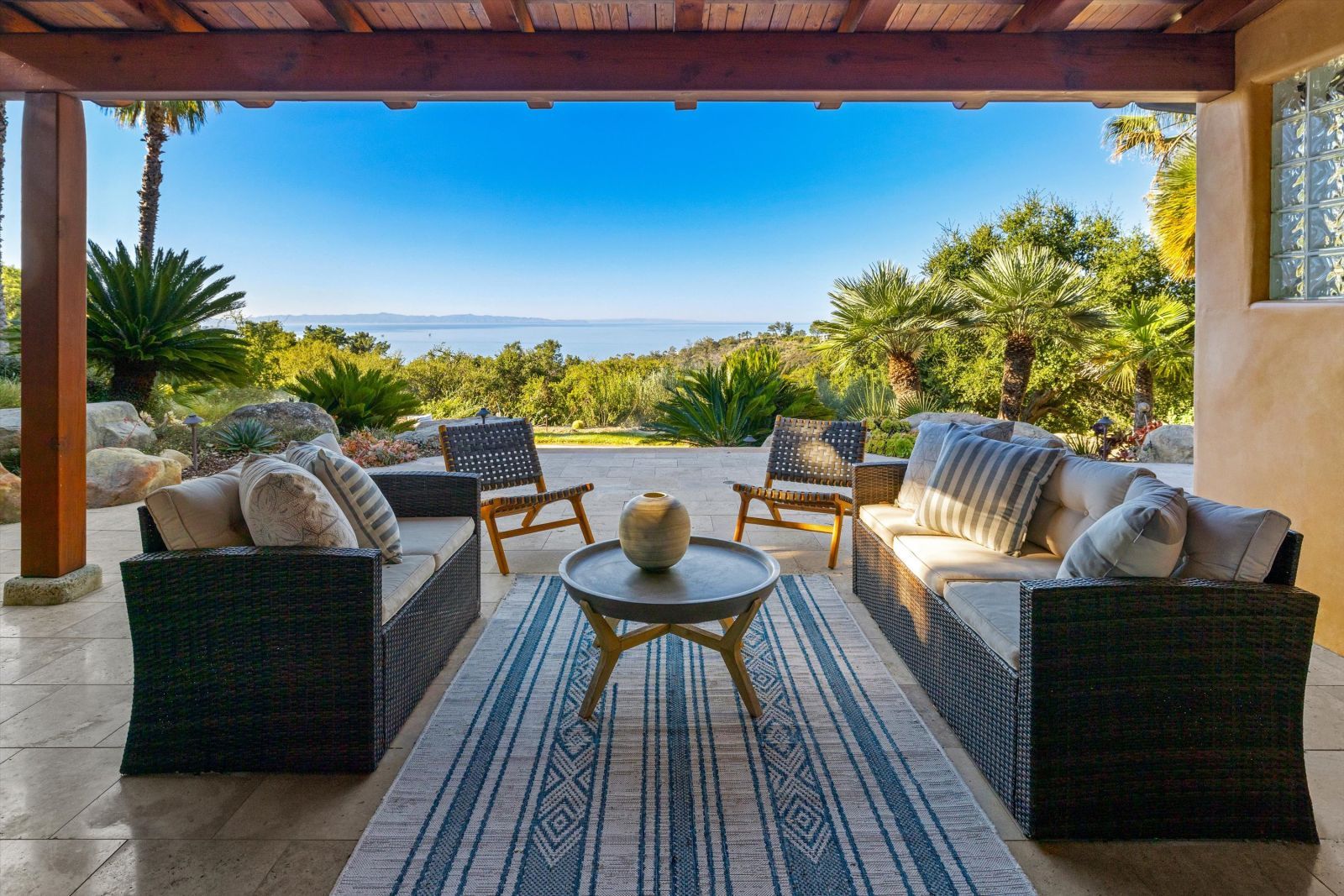 A luxury roofed patio with comfy furniture and an ocean view.