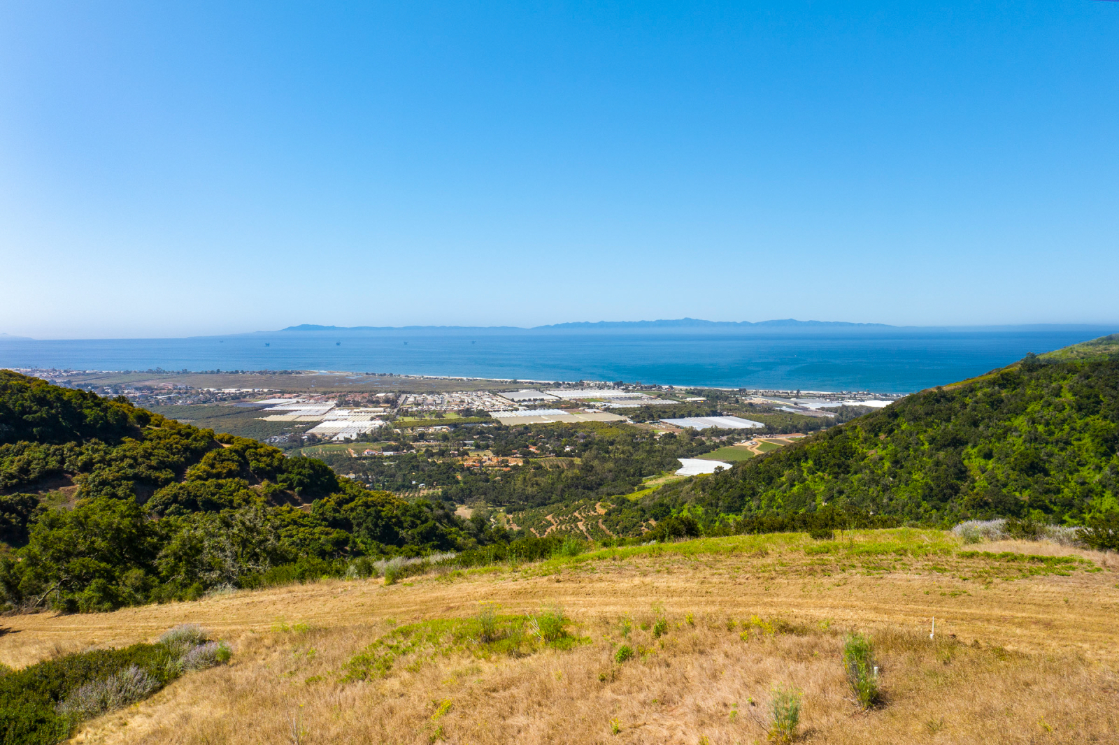Panoramic view from a Carpinteria hillside property featuring rolling coastal terrain, agricultural fields, the Pacific Ocean, and the Channel Islands in the distance.