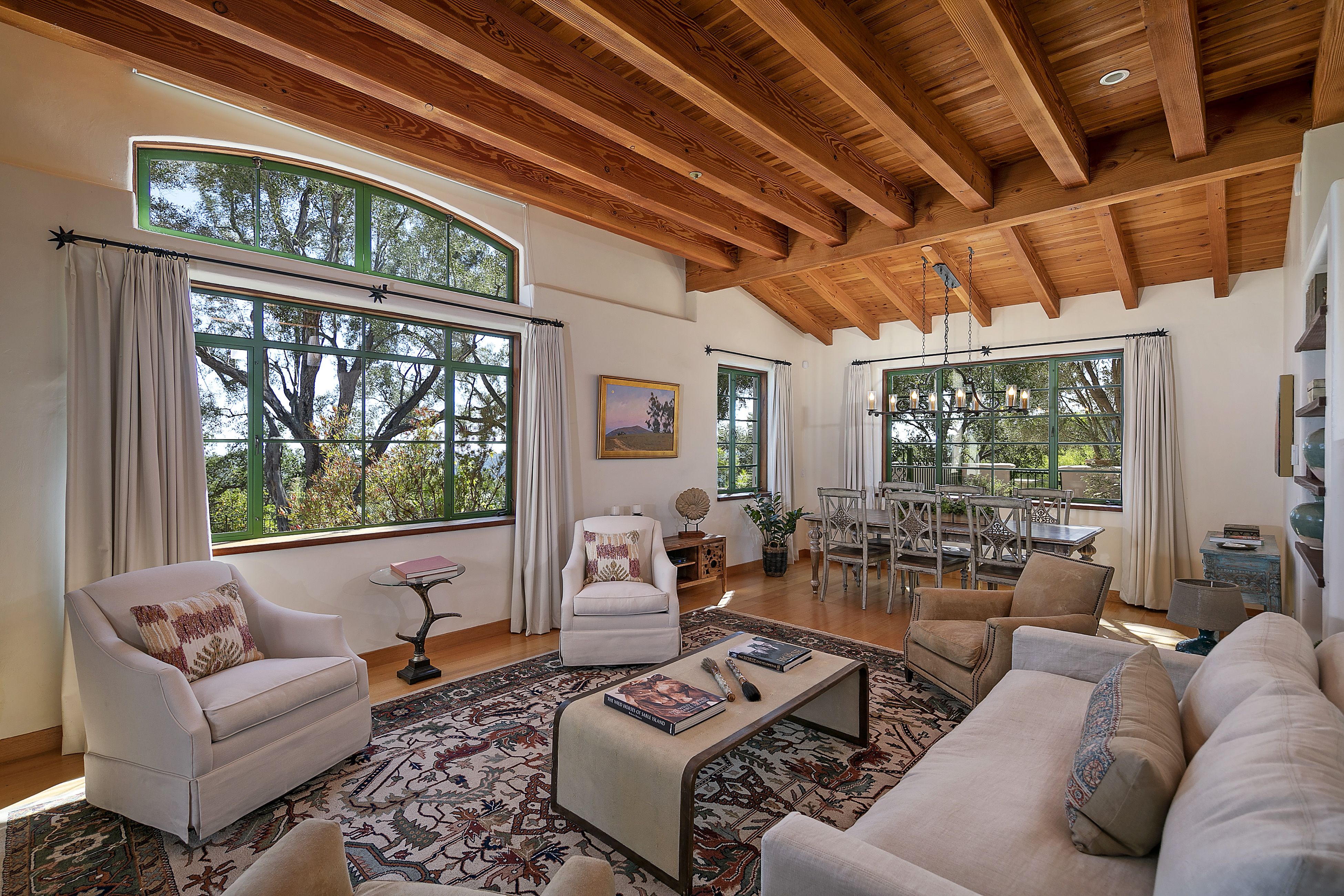 Beautifully furnished living room of a home for sale in Santa Barbara, with an open-beam ceiling and large multi-pane picture windows