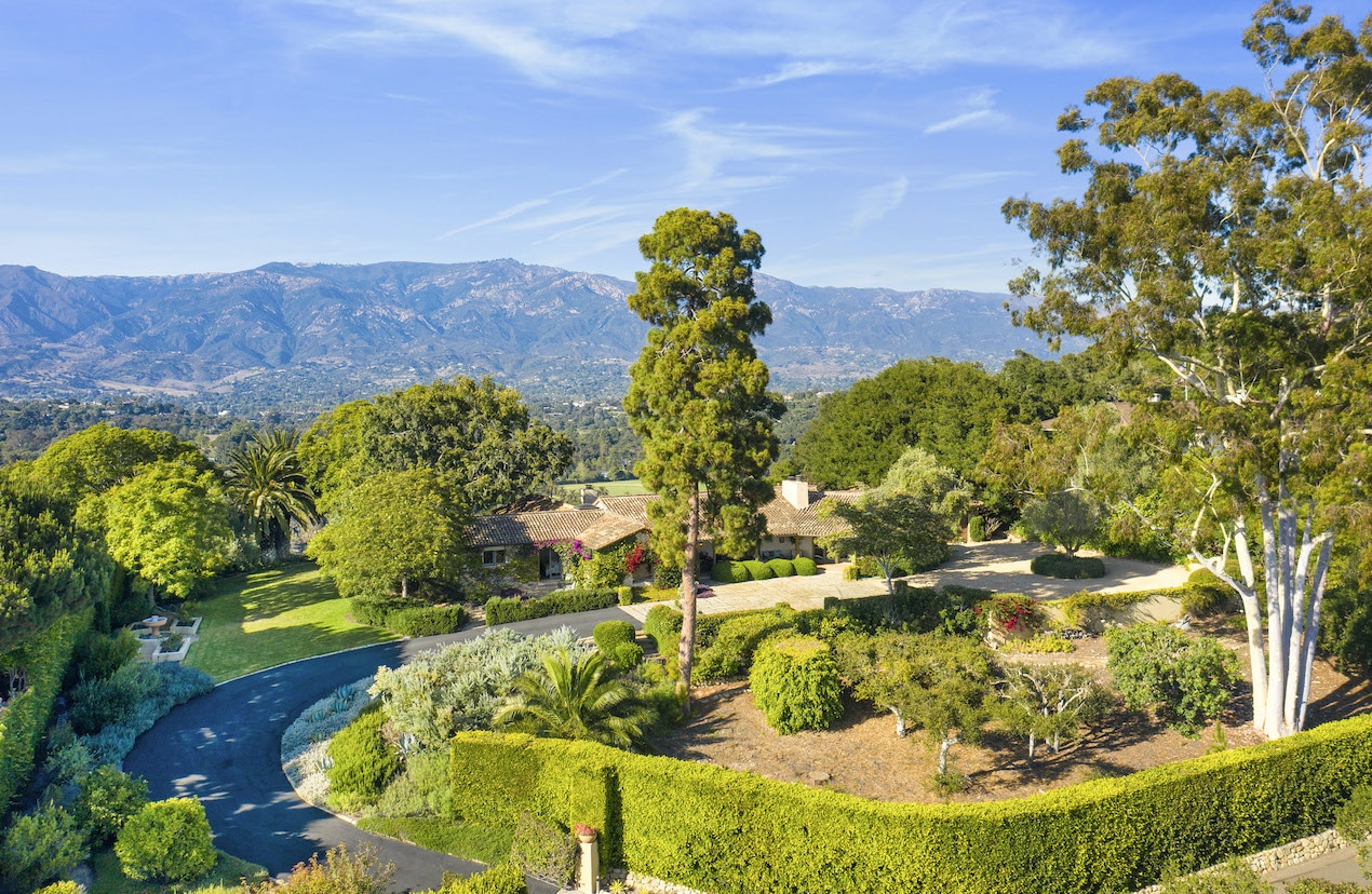 A Hope Ranch estate that;s hidden behind tall trees and landscaping with the mountains in the background
