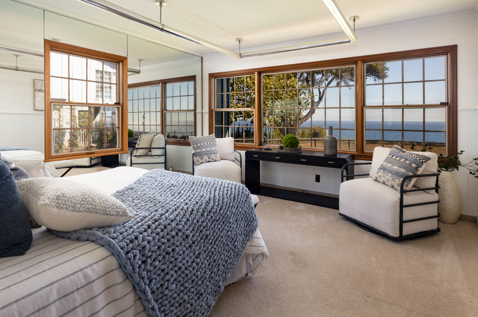 A luxury primary suite with afloor to ceiling windows and the ocean beyond