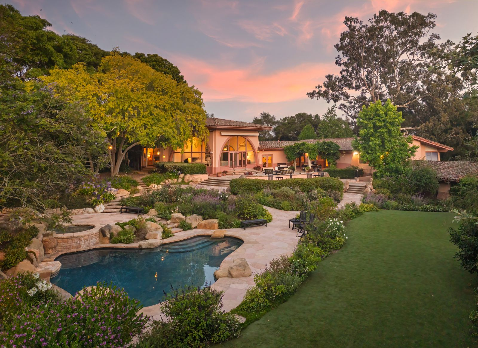 Luxury Hope Ranch estate at sunset featuring a resort-style pool, manicured gardens, expansive lawn, and elegant outdoor living spaces surrounded by mature trees.