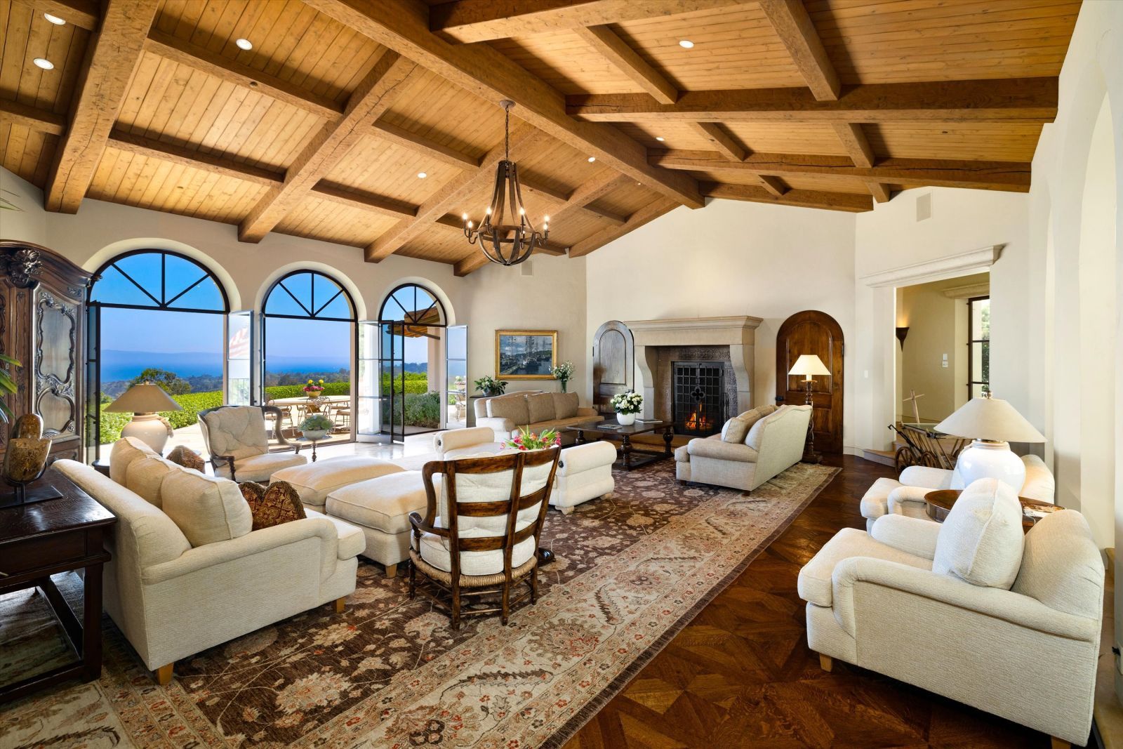Expansive and beautifully furnished living room of a Montecito home, with three large arched windows looking out to an ocean view.