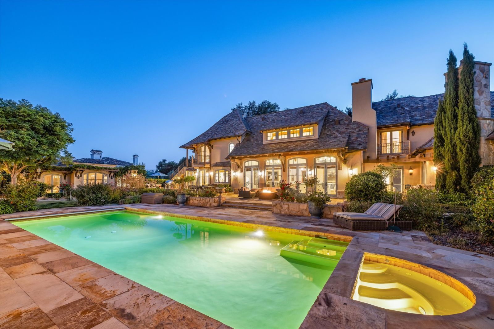 Rear grounds of a large estate home, fully lit inside and outside with sophisticated lighting.