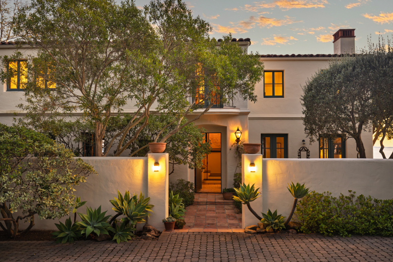 Montecito Spanish-style home with white stucco walls, gated courtyard entry, warm lighting, mature landscaping, and classic Mediterranean design.