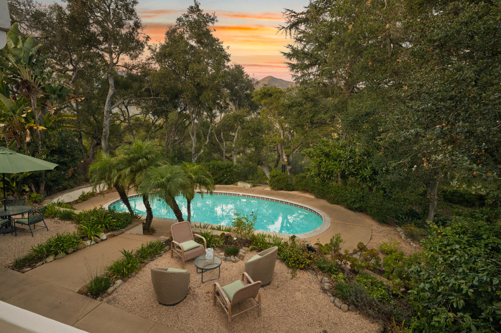 Private Santa Barbara backyard retreat featuring a swimming pool, lounge seating, mature trees, and landscaped gardens with mountain views at sunset.