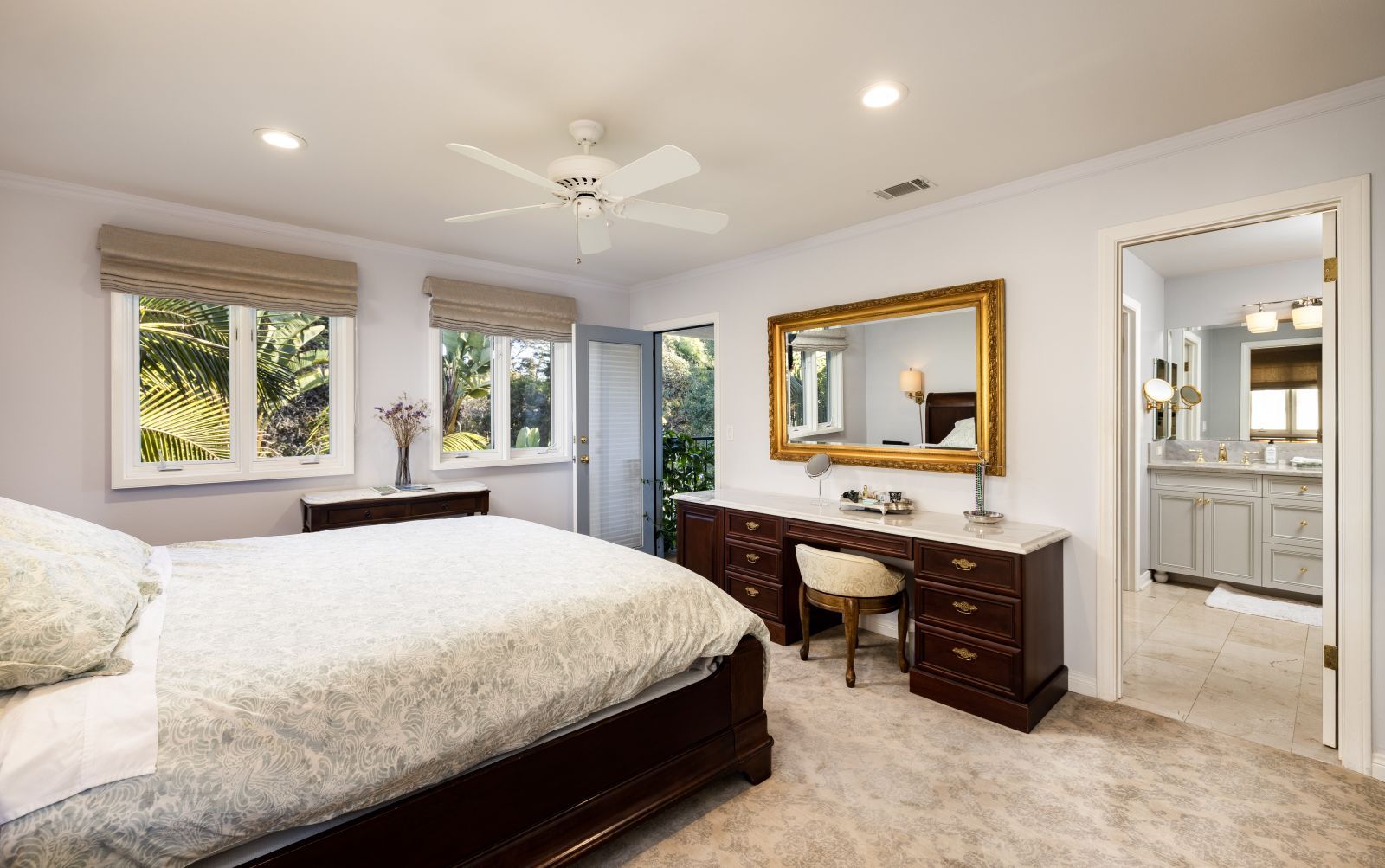 A cozy luxury bedroom with a ceiling fan and a large mirror with an open door leading to the bathroom