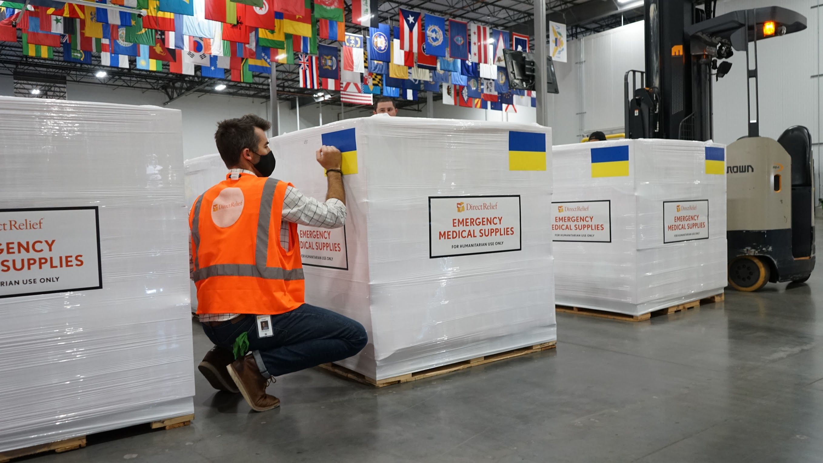 A person in an orange vest next to containers marked Emergency Medical Supplies