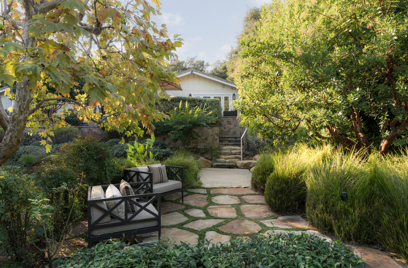 Lush Montecito garden with stone pathways, outdoor seating, mature trees, and a charming home surrounded by greenery.