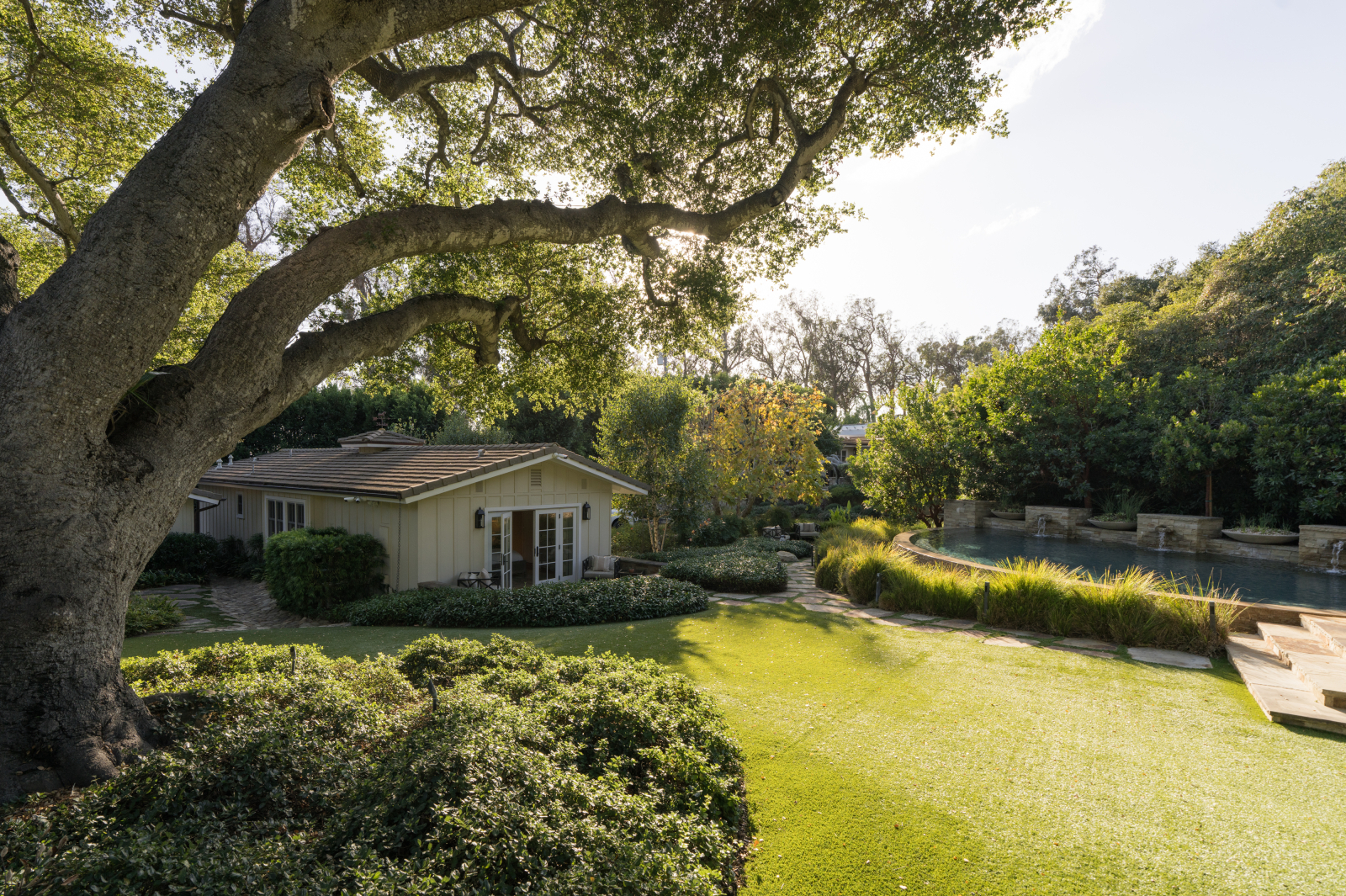 Expansive Montecito backyard with a mature oak tree, manicured lawn, guest house, swimming pool, and lush landscaping.