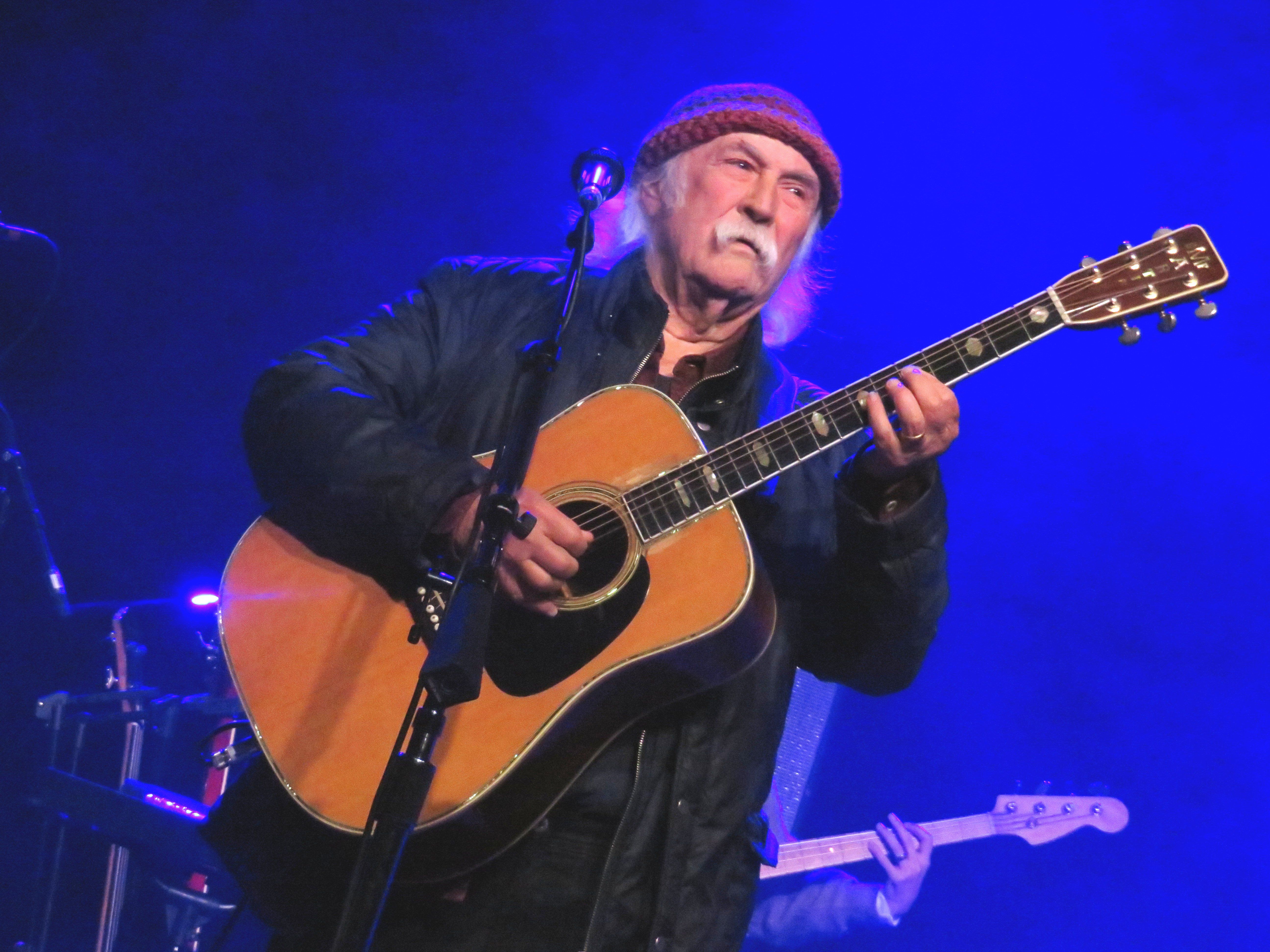 The legendary David Crosby playing his guitar with a blue background