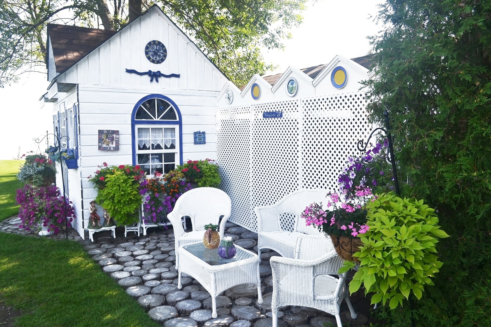 A beautiful small shed with nice chairs and a lot of flowers in the backyard, painted new in white.
