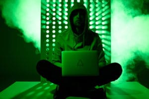 Hacker with laptop in front of green technology looking wall to illustrate technology and privacy