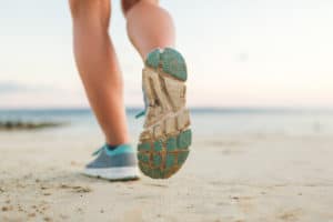 Close up of a person in tennis shoes running along the beach