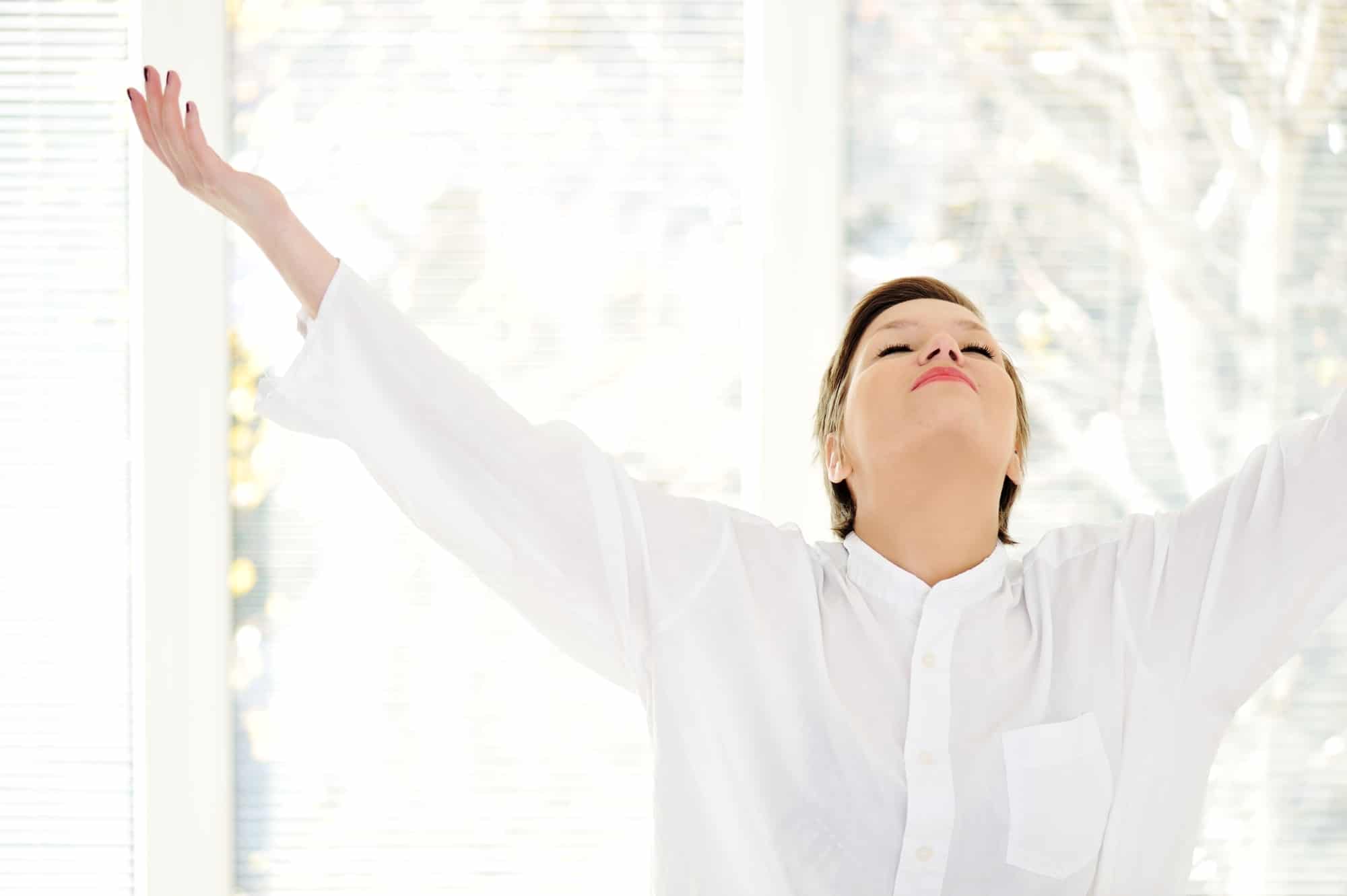 Relaxed young woman at home with raised arms