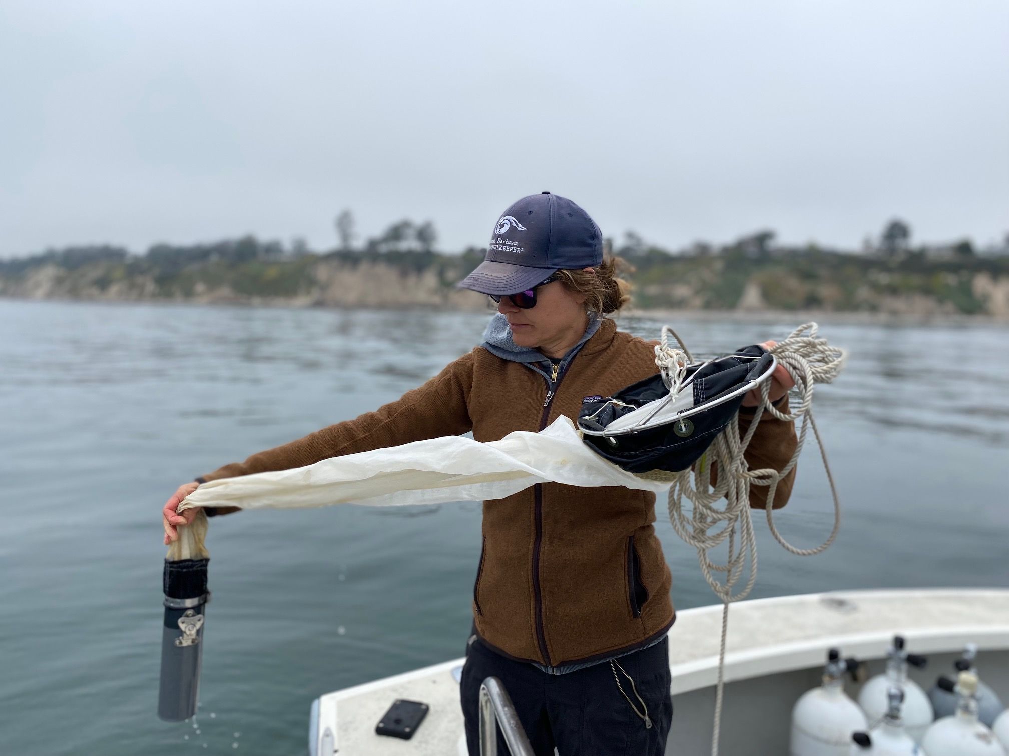 Woman in a jacket and baseball cap taking a plankton sample with an instrument takes plankton readings