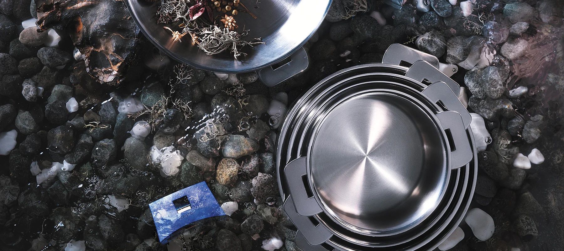 A top view of stainless steel cooking pots nesting in each other on a bed of black rocks