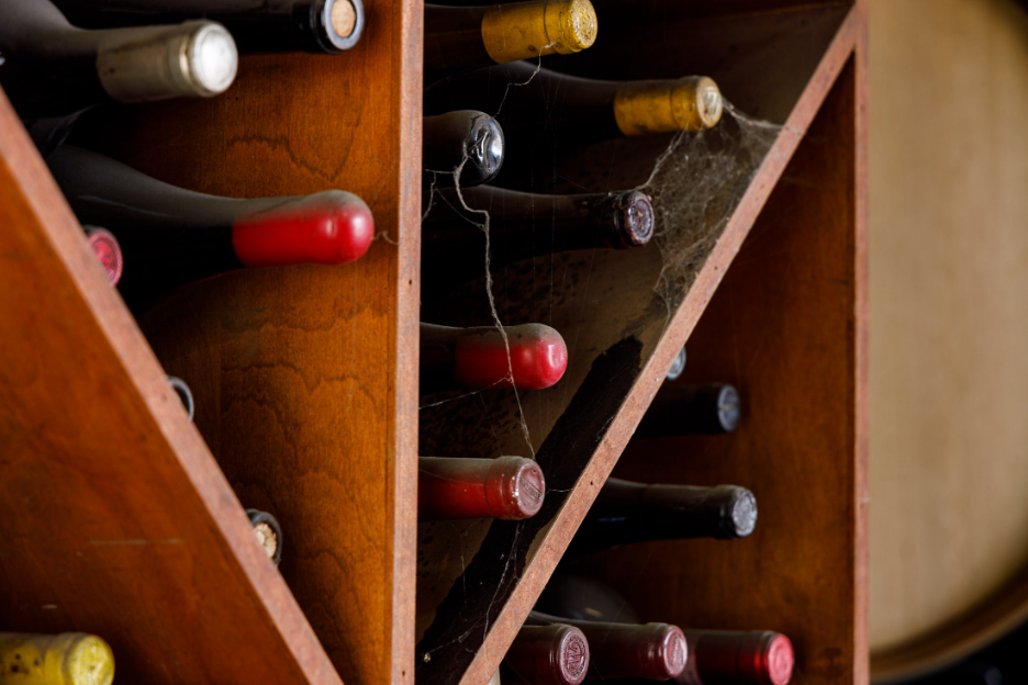 Shelves in a wine cellar, containing a couple dozen dusty unopened wine bottles laying on their sides.