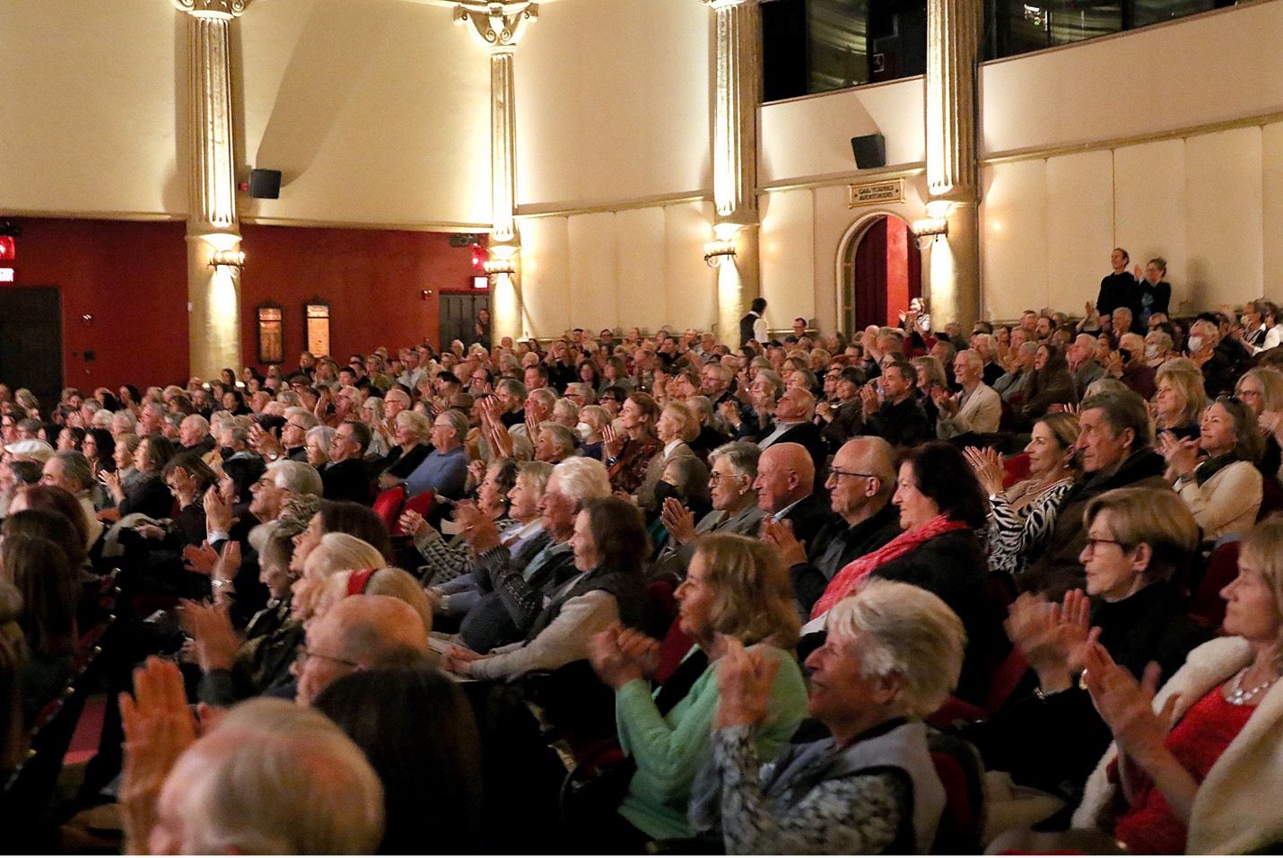 A full audience inside a theater with everyone looking at the stage in front of them.